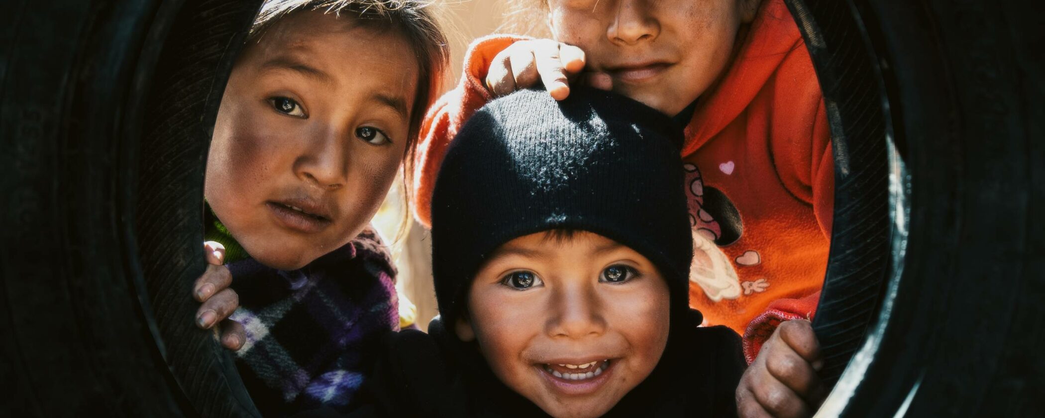 Three children peek through the gap in an old truck tyre