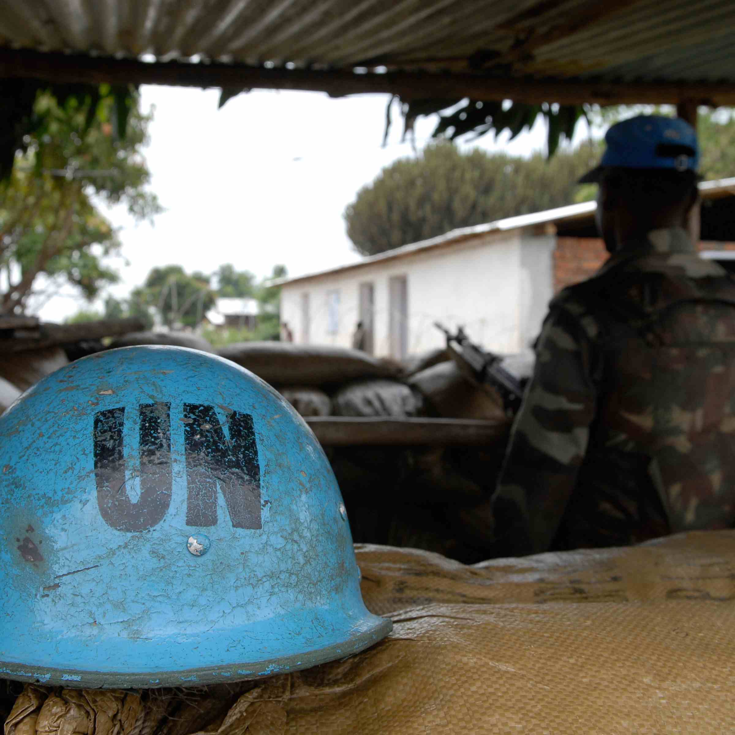 Picture shows a blue helmet marked with the letters 'UN'. In the background is soldier wearing camouflage.