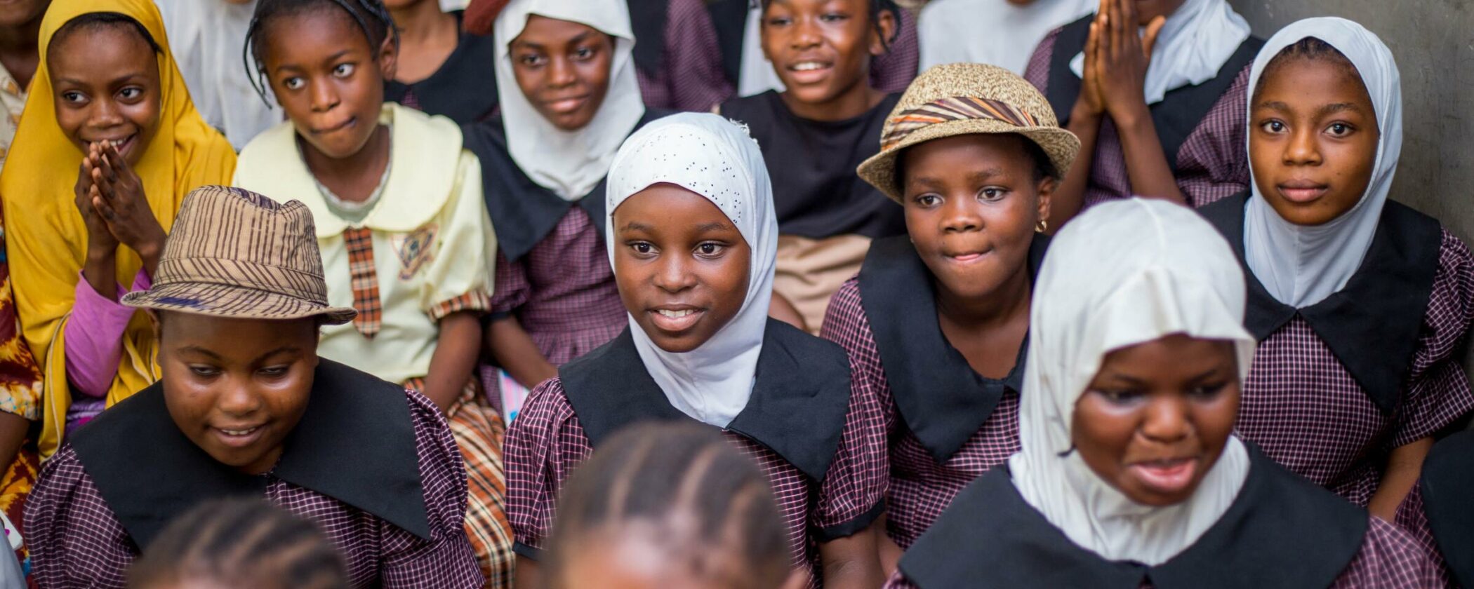 A group of children, adorned with hats and headscarves, some are smiling. 