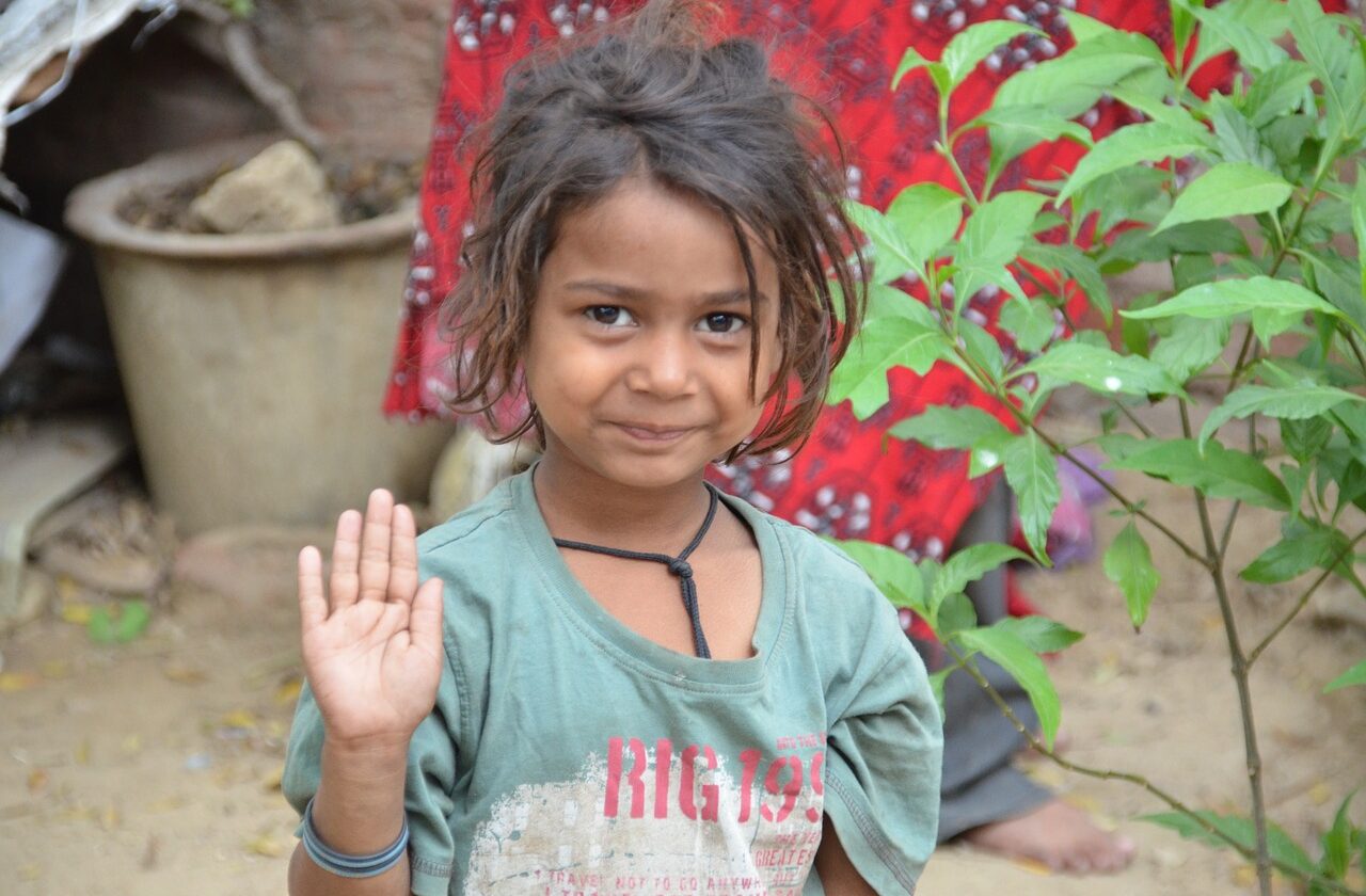 Child smiling and holding up her hand in a wave.